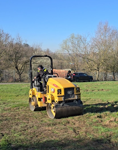 Rolling the soil or lawn surface using a garden roller to level and compact the ground.